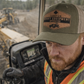 Person wearing a 'Canadian Heavy Equipment Operator' cap in front of construction equipment.