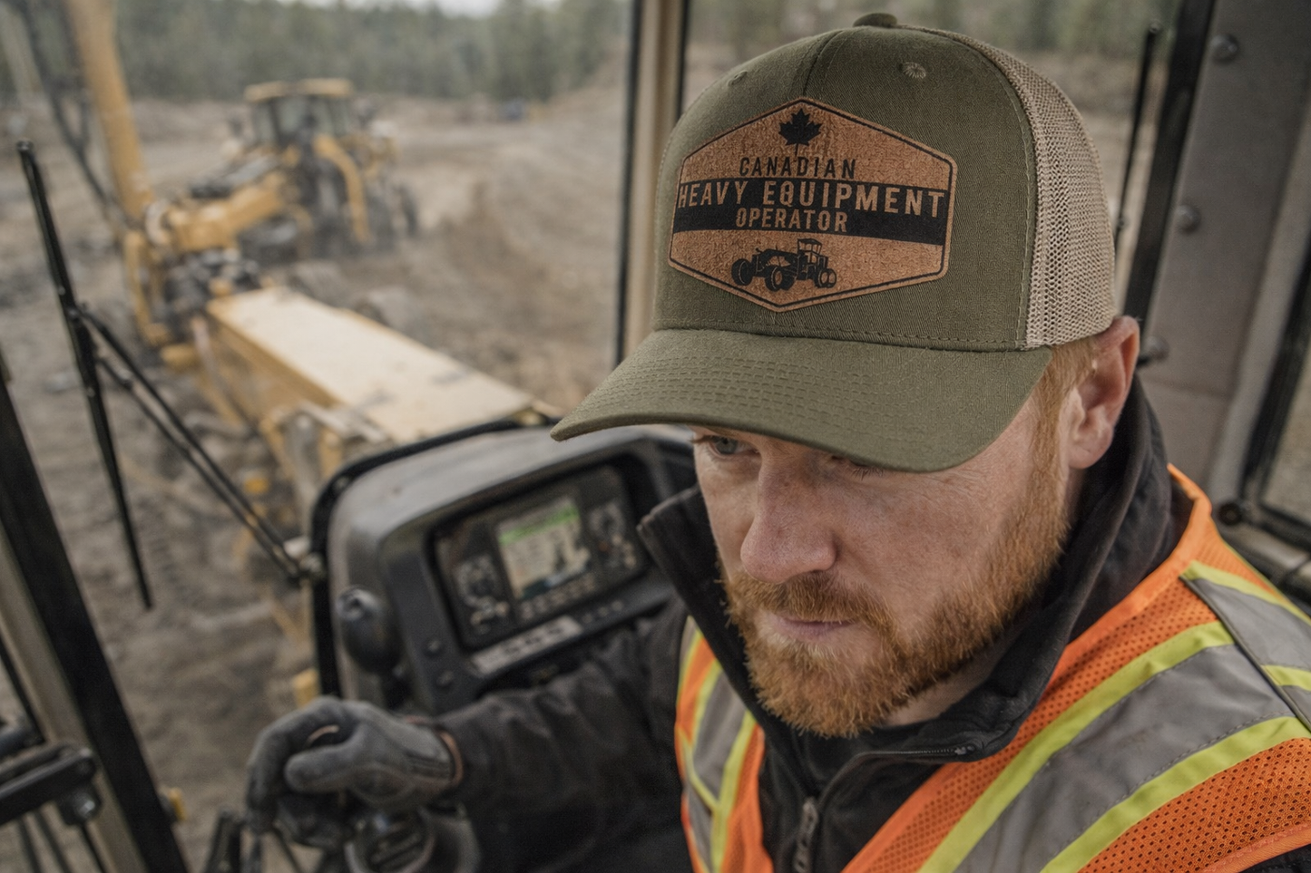 Person wearing a 'Canadian Heavy Equipment Operator' cap in front of construction equipment.