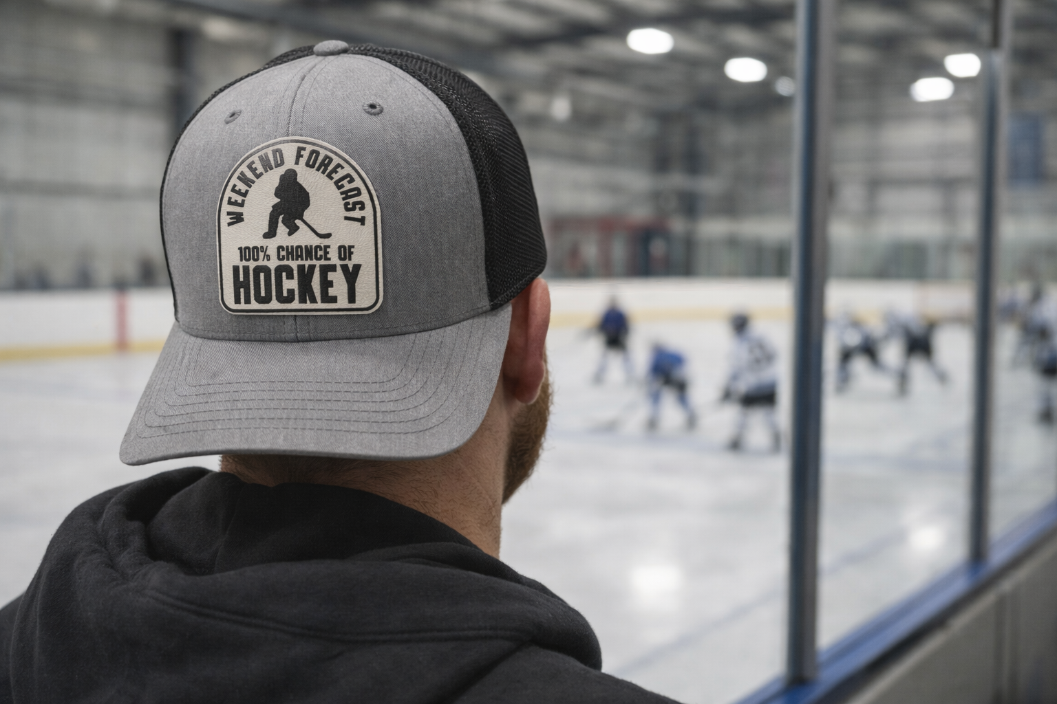 Person wearing a cap with 'Weekend Forecast 100% Chance of Hockey' text, looking at an ice hockey rink.