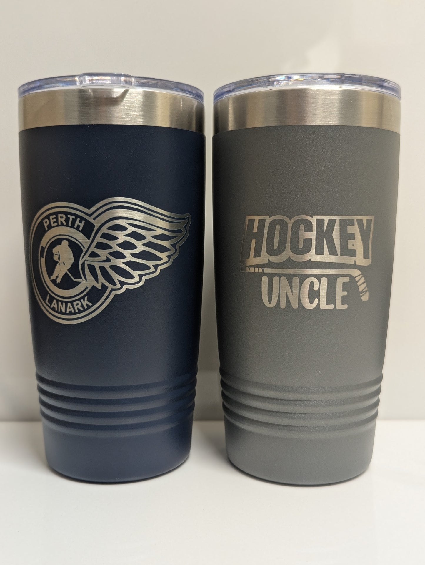 Two tumblers, one navy and one gray, with engraved text and logos on a white background.